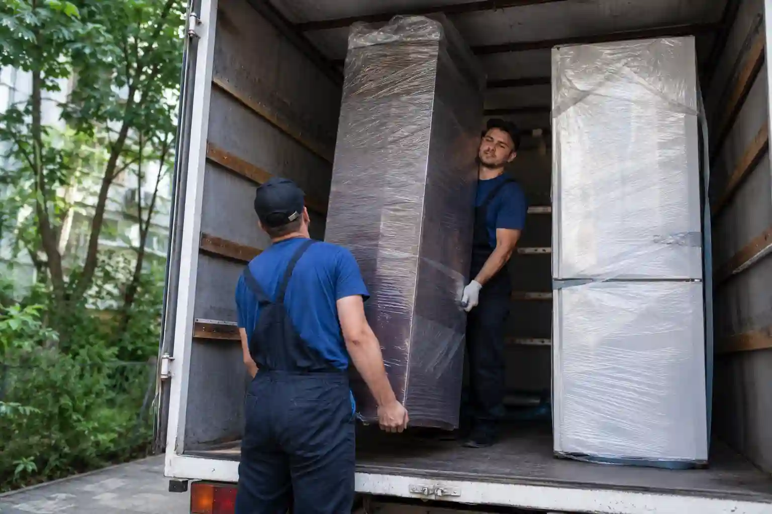 Перевезення великогабаритних меблів: вантажники заносять шафу в кузов вантажівки